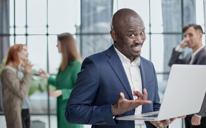 Young african american man in business suit holding laptop while standing at office corridor